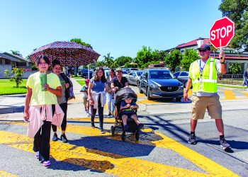 A group of people walking across the street with the help of a crossing guard