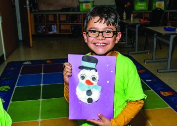 A young boy holds a photo of a snowman that he made himself